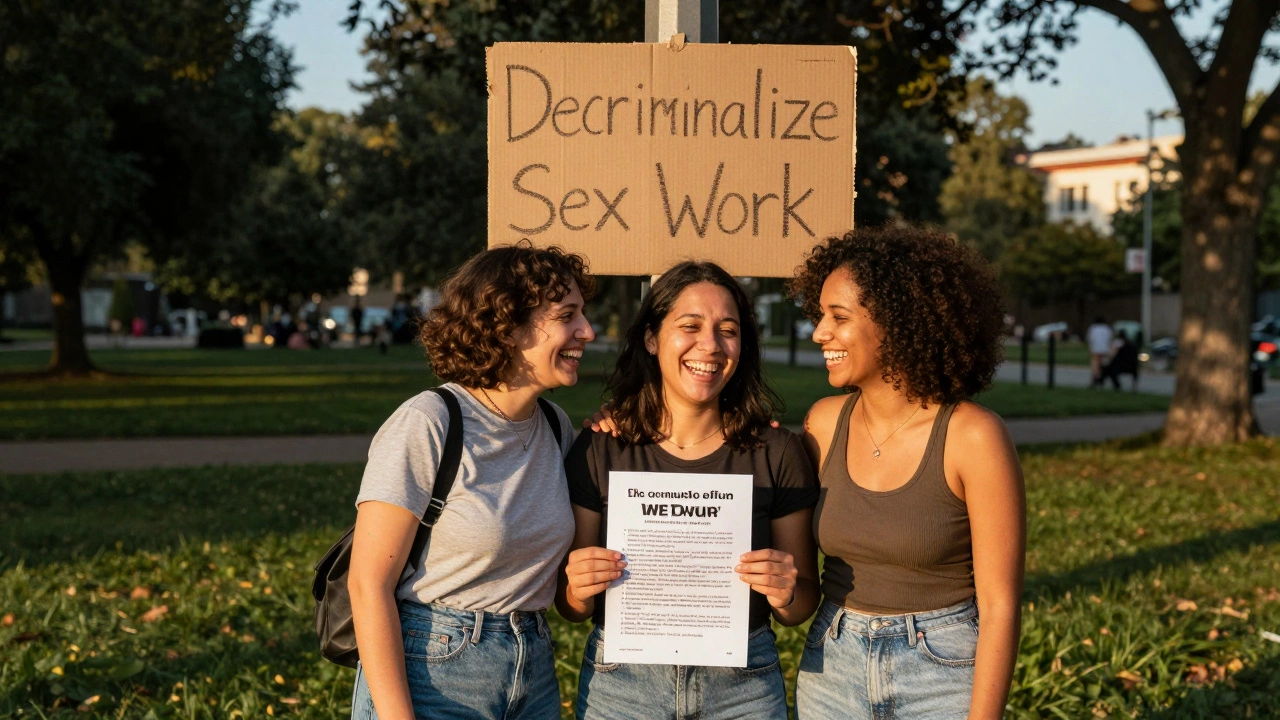 Three women of colour laughing together in a park at sunset, with a faint &#039;Decriminalize Sex Work&#039; sign in the background.